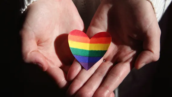 hands holding a heart colored like a pride flag